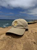 Wild Flower Cap khaki dad hat resting on sunlit beach rocks by the ocean